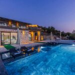 Elegant stone villa with infinity pool offers serene vacation vibes at twilight.